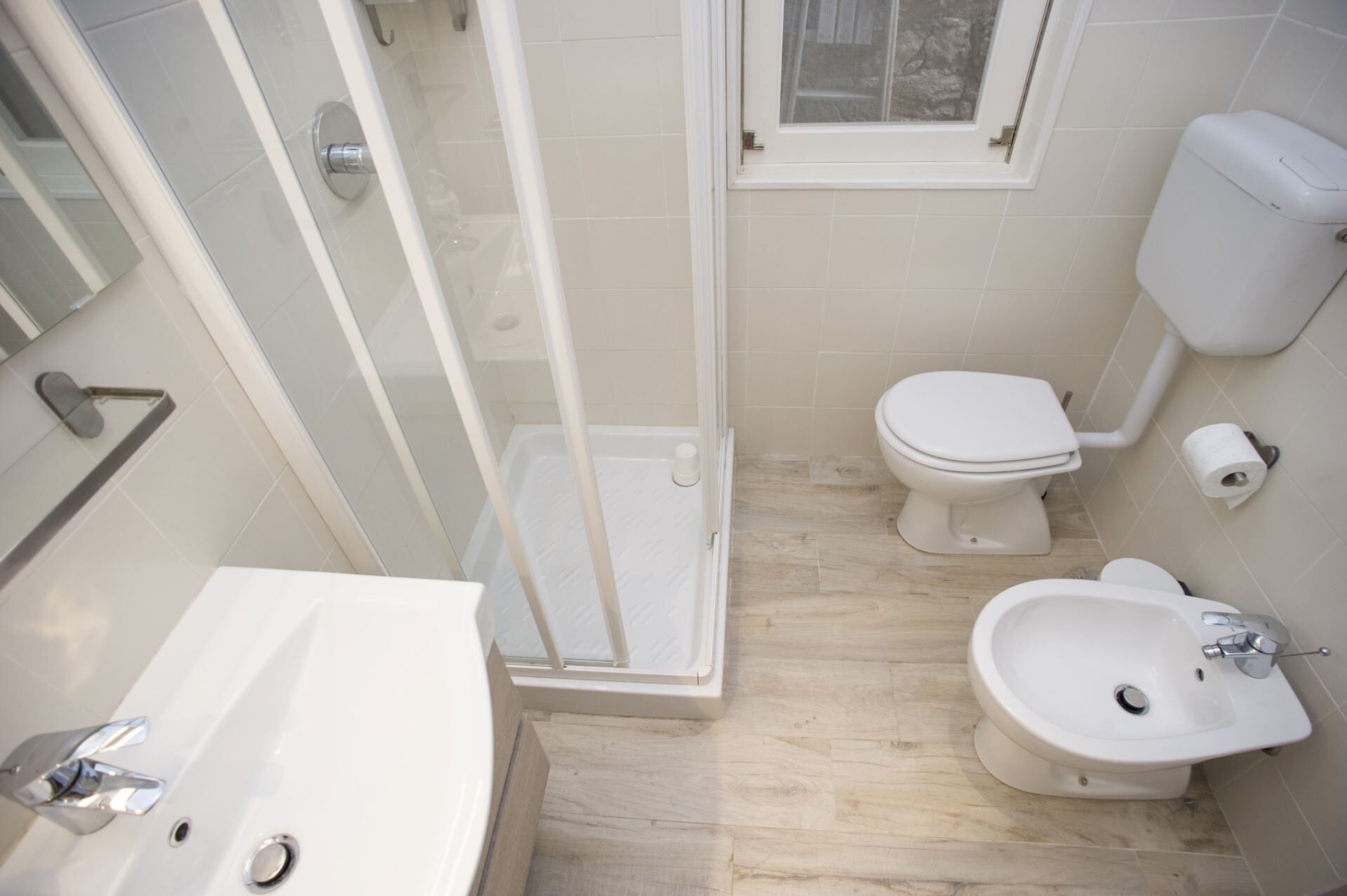A bathroom with a shower, toilet, bidet, and sink.