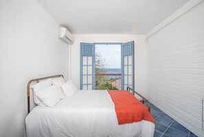 Een slaapkamer met een bed, witte muren, uitzicht door openslaande luiken en een balkon.