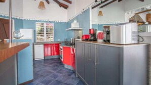 Cucina con mobili rossi e grigi, frigorifero bianco, macchina del caffè rossa e finestra vista giardino.
