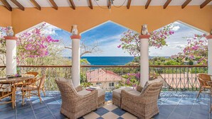 A covered patio with wicker furniture, a dining table, and a view of the sea and greenery. - Villa Sol y Sombra the Cuban spirit (Schoelcher)