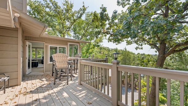 A wooden deck with Adirondack chairs, a railing, and a view of trees. - Margaritaville Luxurious Lakeview Living (Osage Beach)
