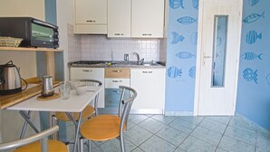 A compact kitchen with white cabinets, a microwave, a kettle, and a dining area with a table and chairs. - Punta Contessa - Punta Contessa n°4 (Capoliveri)