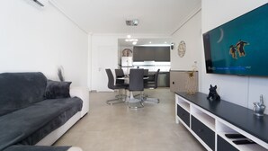 A modern living room with a grey sofa, a dining area with a table and chairs, and a TV mounted on the wall. - Apartment Casa Titan (Riomar) (Pilar de la Horadada)