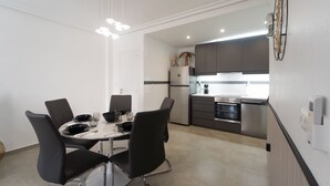 A modern kitchen with a dining area, featuring a marble table, black chairs, and stainless steel appliances. - Apartment Casa Titan (Riomar) (Pilar de la Horadada)