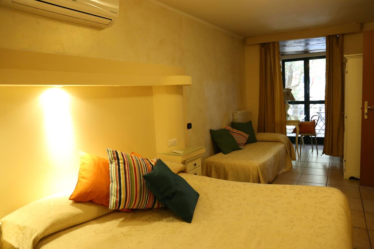 A hotel room with two beds, a nightstand, a chair, and a view of the outdoors.