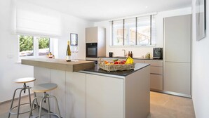 Una cocina moderna con una isla central, taburetes de bar, una botella de vino y una cesta de fruta.
