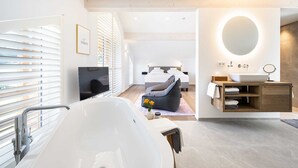 Un baño moderno con bañera, tocador con espejo y una cama al fondo.