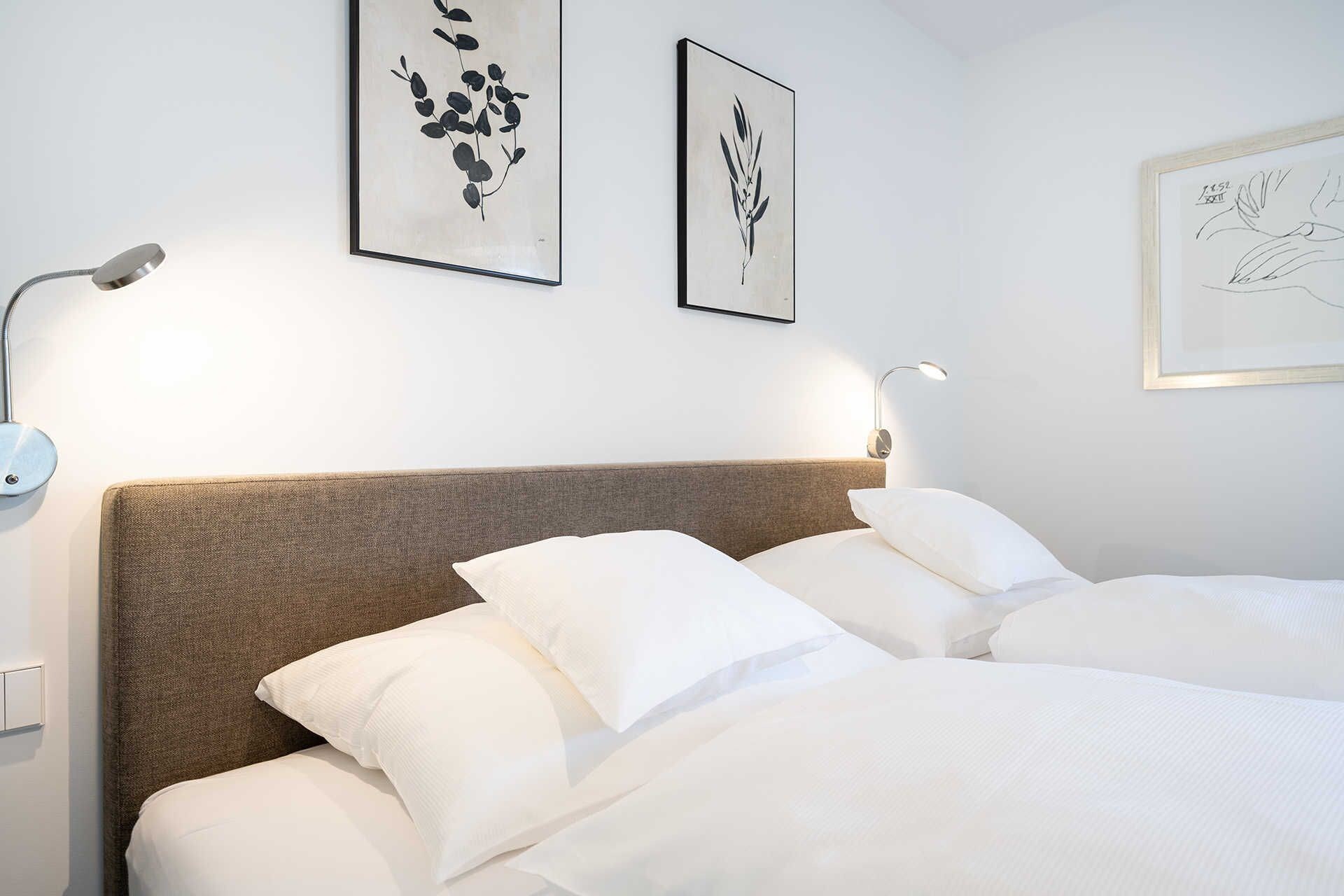A neatly made bed with white linens, a brown headboard, and two wall-mounted light fixtures.