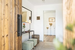 A hallway with a wooden door, a mirror, a vase with flowers, a small table with a book, and a wicker basket.