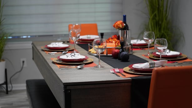Une table à manger dressée avec de l’argenterie rouge et dorée, des verres transparents et une bouteille de vin.