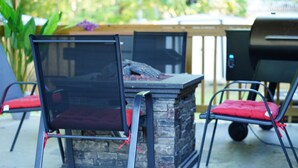 Un espace patio agrémenté d’une cheminée en pierre, de chaises en métal avec des coussins rouges et d’un barbecue.