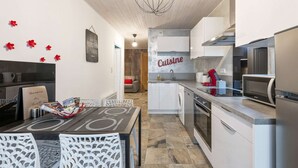 A modern kitchen with white cabinetry, a dining area with a table and chairs, and a 'Cuisine' sign on the wall.