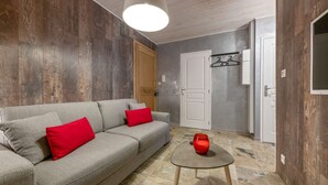 A living room with a grey sofa, red cushions, a small round table with a red vase, and a wooden ceiling.