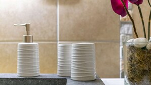 Ett badrum med modern design, utrustat med en tvåldispenser, staplade hygienartiklar och en glasbehållare med dekorativa stenar och en rosa orkidé.