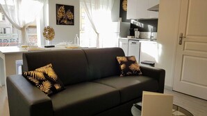 A modern living room with a black sofa, two decorative pillows, a glass coffee table, and a view of a kitchen area. - ★ Bright ★ Quiet ★ City centre ★ Easy Parking ★ WIFI ★ (Le Puy en Velay)