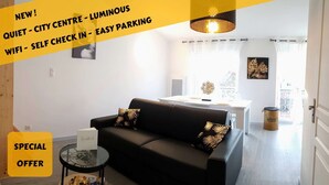 A modern living room with a black sofa, a glass coffee table, and a dining area with a white table and chairs. - ★ Bright ★ Quiet ★ City centre ★ Easy Parking ★ WIFI ★ (Le Puy en Velay)