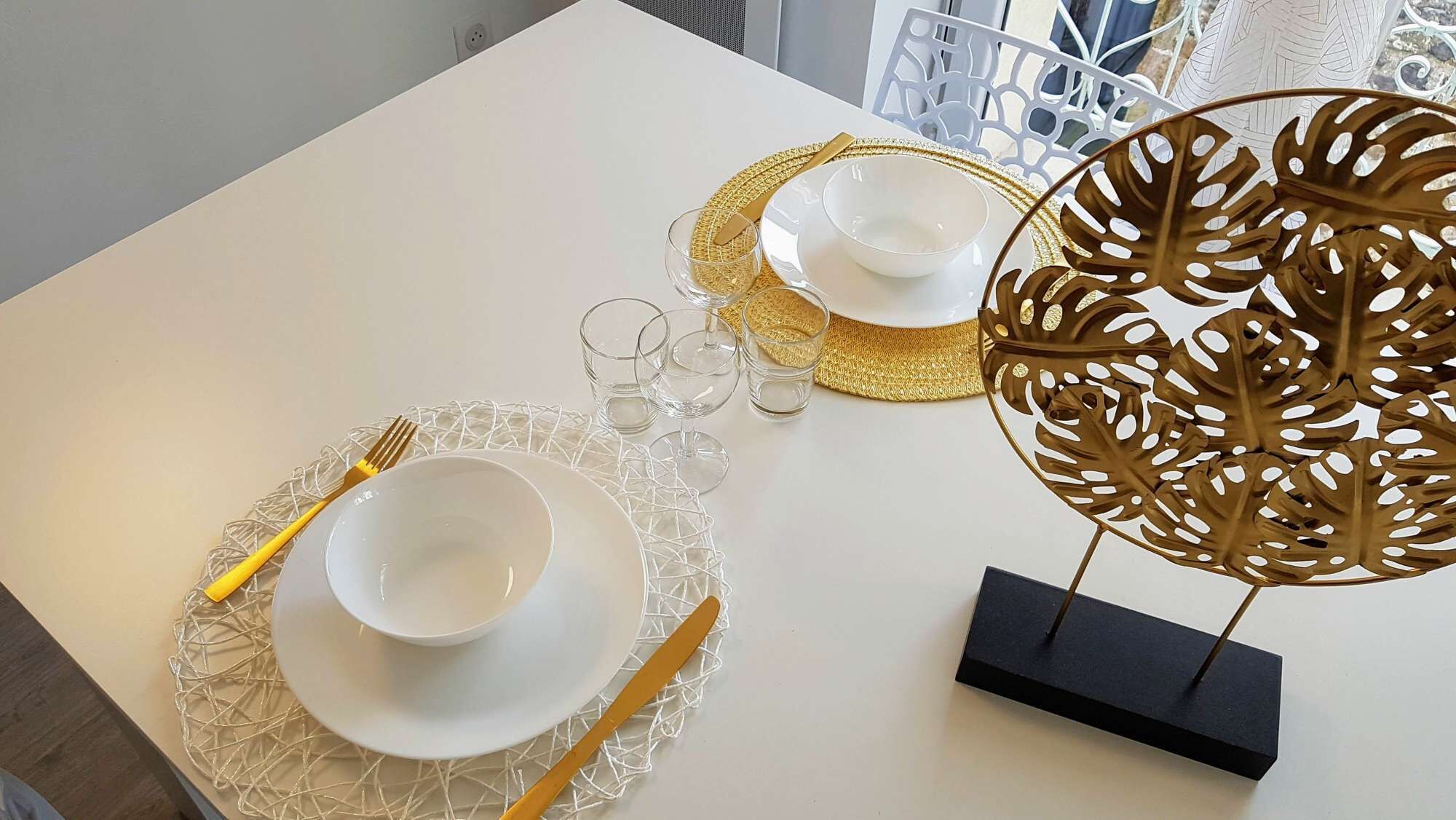 A table set with white plates, gold cutlery, and clear glasses, accompanied by a decorative leaf-shaped centerpiece.