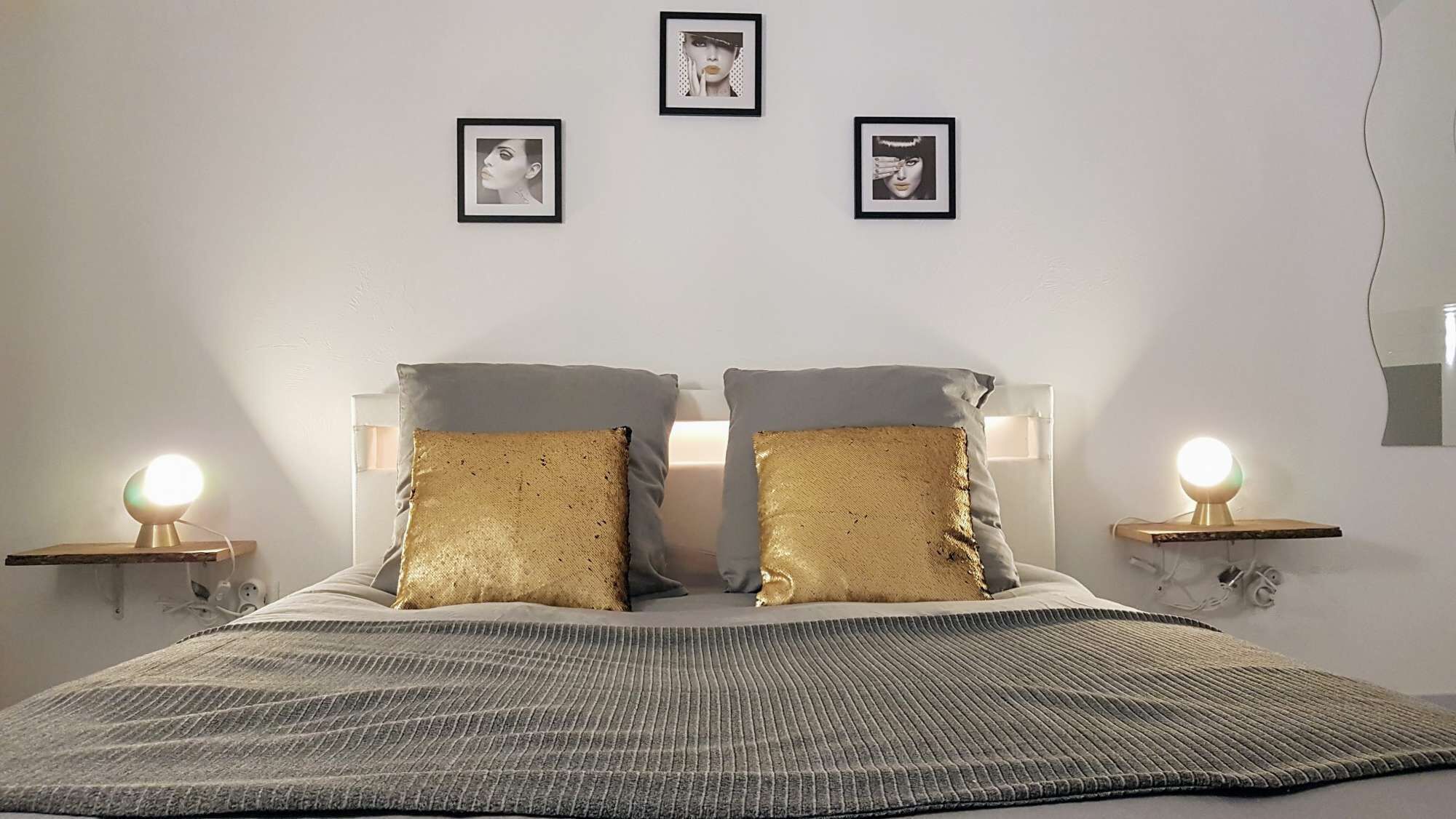 Een keurig opgemaakt slaapkamer met een bed, twee nachtkastjes met lampen, en drie ingelijste foto's aan de muur.