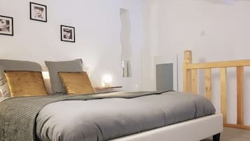 Ein Schlafzimmer mit einem Bett, Kissen, einem Nachttisch mit Lampe und gerahmten Bildern an der Wand.