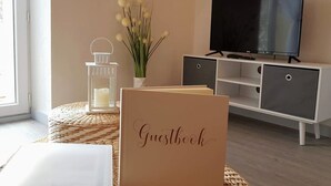 Una sala de estar moderna con un televisor de pantalla plana, un libro de visitas, una vela y un florero con flores.