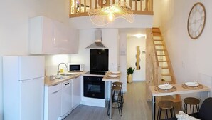Una cocina moderna con armarios blancos, una estufa negra y un microondas. Se ve una escalera de madera que lleva a un comedor con una mesa lista para dos.
