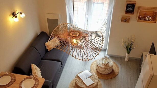 Una sala de estar acogedora con un sofá oscuro, una lámpara colgante de fibras tejidas y dos mesitas redondas con individuales.