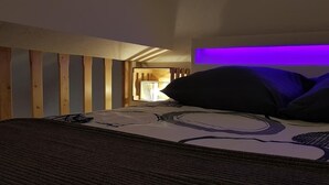Un dormitorio con cama, listones de madera en la pared y una tira de luz morada sobre la cama.