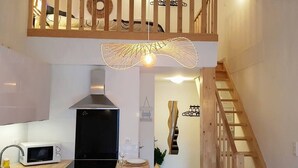 Una cocina moderna con microondas, estufa y lavaplatos. Se observa una escalera de madera y una lámpara decorativa.