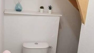 Une petite salle de bain propre, avec des toilettes blanches, une petite étagère ornée de plantes et un escalier en bois.