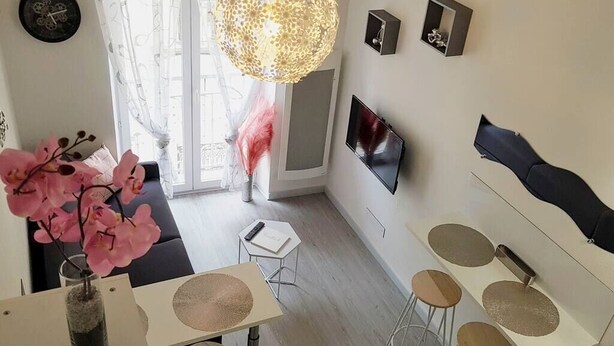 Una sala moderna con televisor, un comedor con taburetes y un ventanal con cortinas.