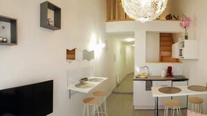 Una cocina moderna con televisión de pantalla plana, encimeras blancas y taburetes de bar.