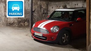 Un Mini Cooper rojo estacionado en un garaje de concreto con un letrero que dice 'PARKING'.