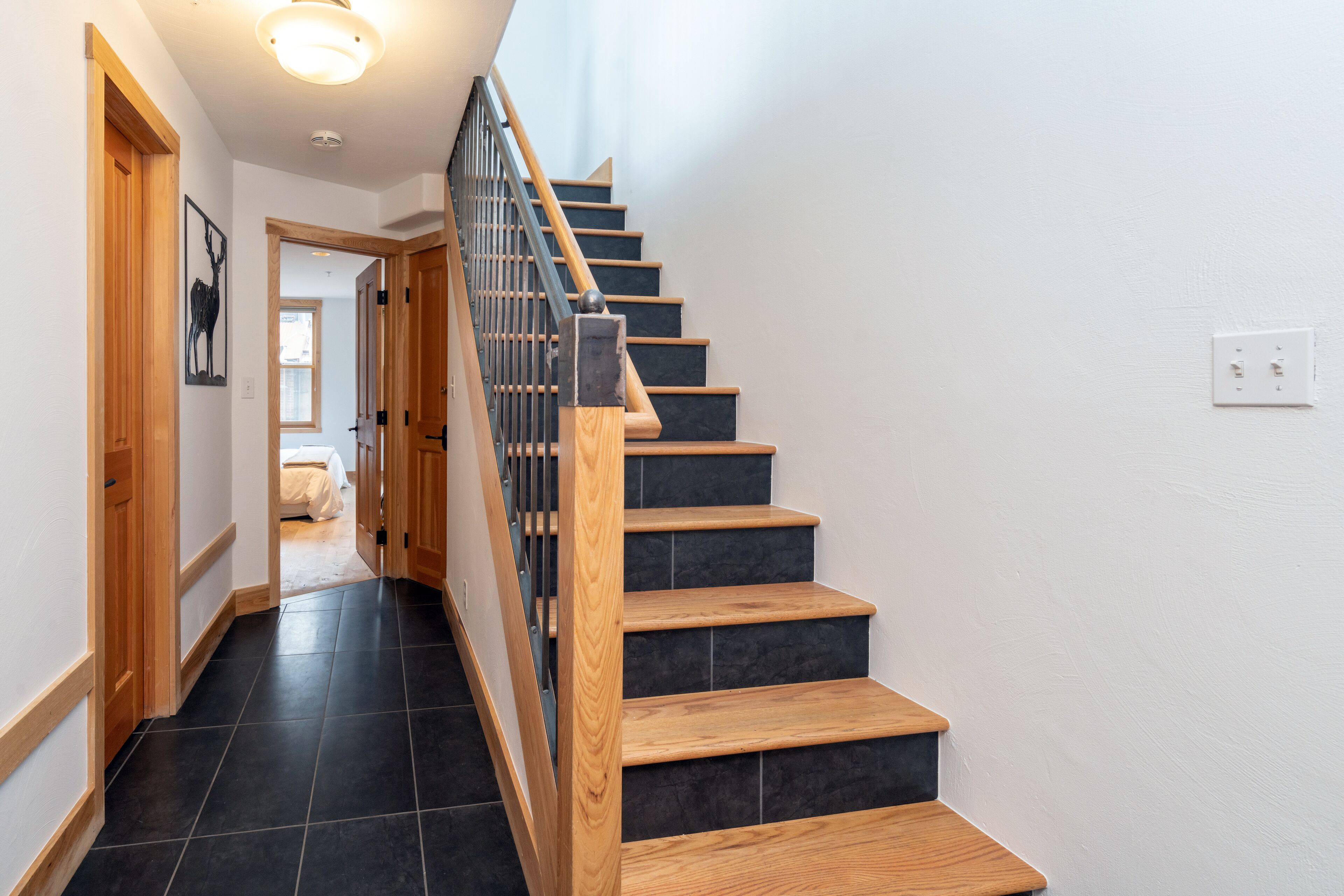 A staircase with wooden steps and a metal railing, leading to a bedroom with a bed and a window.