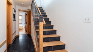 Una escalera de madera con barandilla de metal que lleva a un dormitorio con cama y ventana.