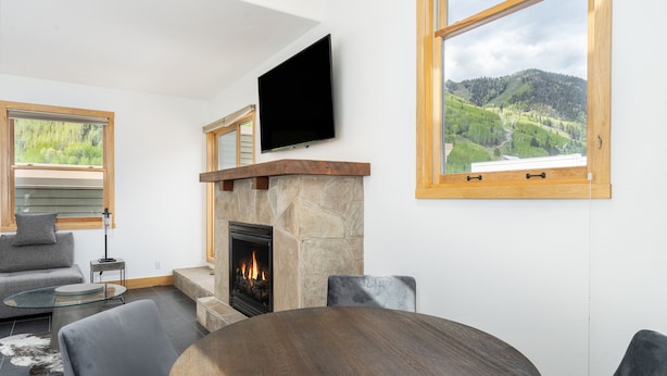 Una sala de estar moderna con chimenea de piedra, un televisor de pantalla plana montado encima y un amplio ventanal con vistas a un paisaje montañoso.