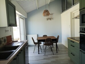 Una cocina moderna con comedor, que incluye una mesa y sillas de madera, una lámpara colgante y electrodomésticos integrados.