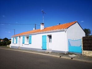 Una casa blanca con contraventanas azules y techo de tejas rojas.