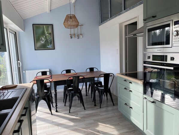 A modern kitchen with a dining area, featuring a wooden table, black chairs, and a hanging light fixture.