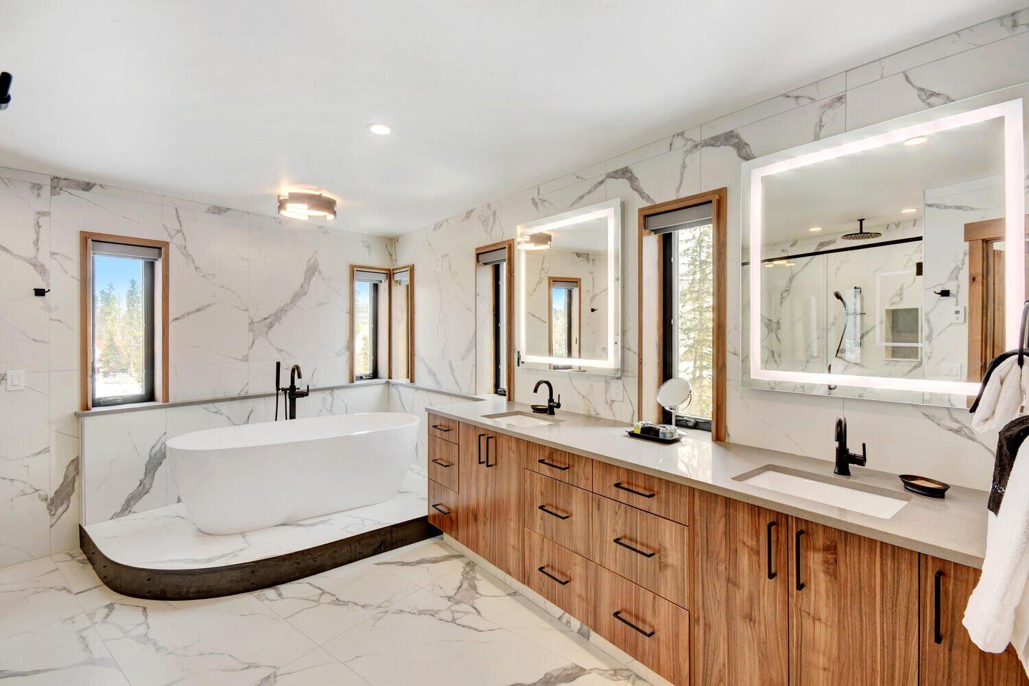 A modern bathroom with a freestanding bathtub, wooden cabinetry, and large mirrors.