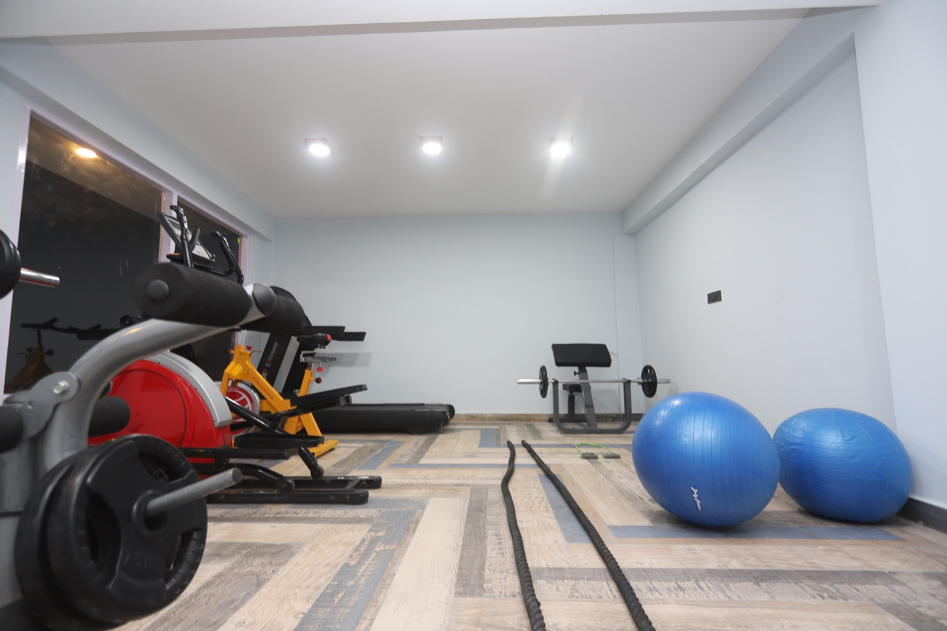 A gym with exercise equipment, including a red stationary bike, a yellow bike, a bench press, and two blue exercise balls.