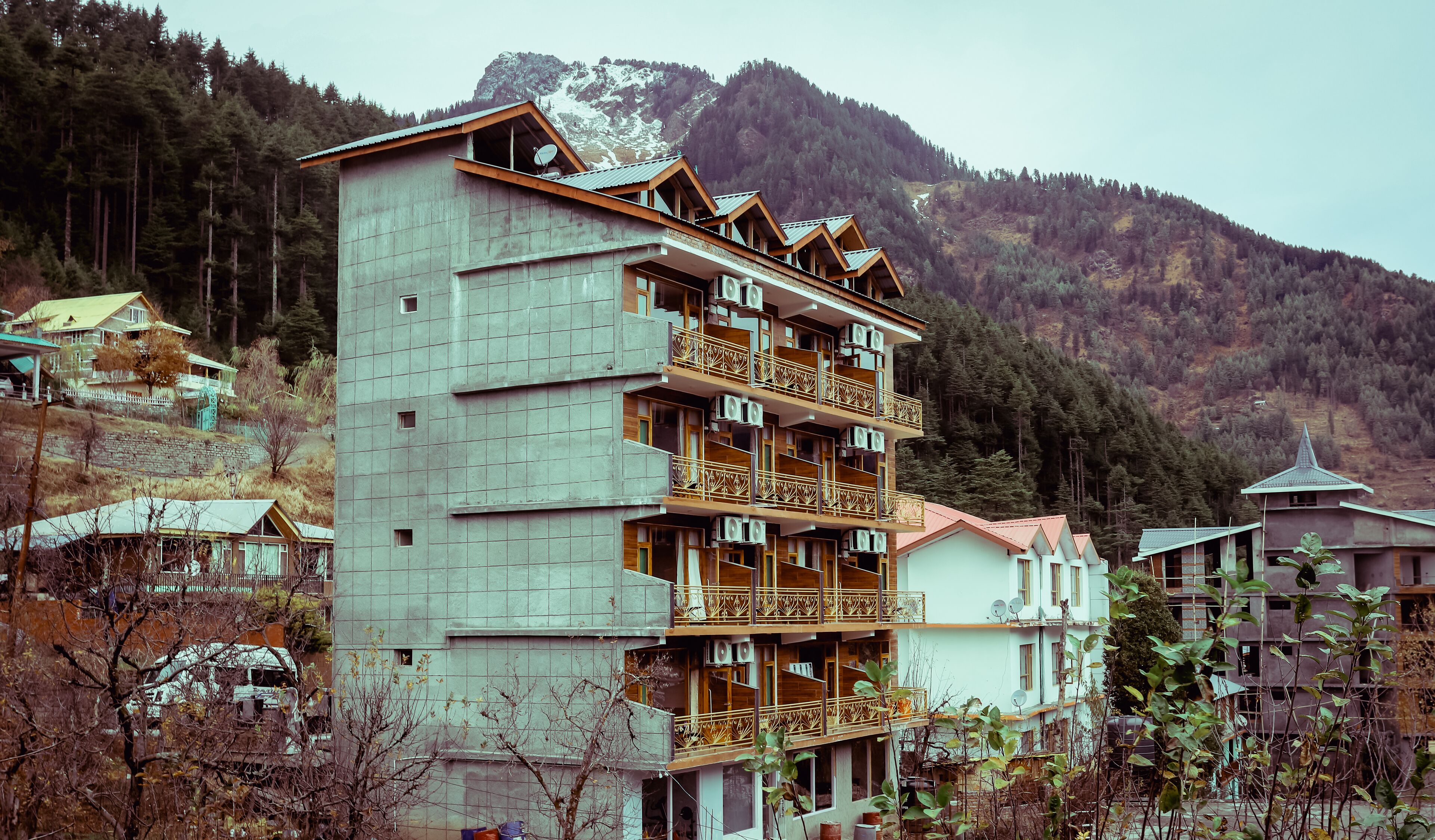 A multi-story hotel with balconies, a mountainous backdrop, and a mix of modern and traditional architecture.