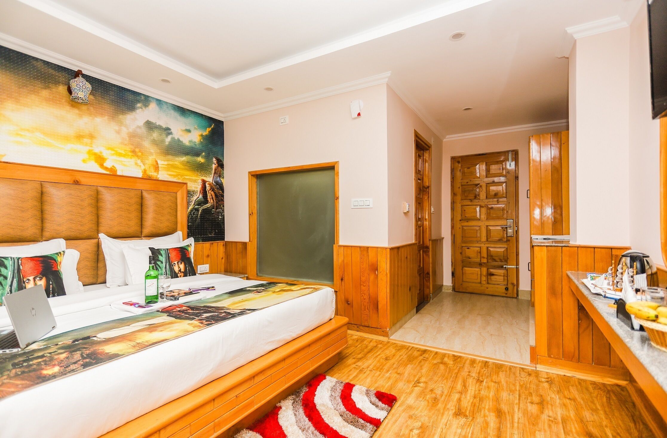 Ein Hotelzimmer mit einem Bett, einem Schreibtisch mit Computer, einem Bild an der Wand und einer Holztür.
