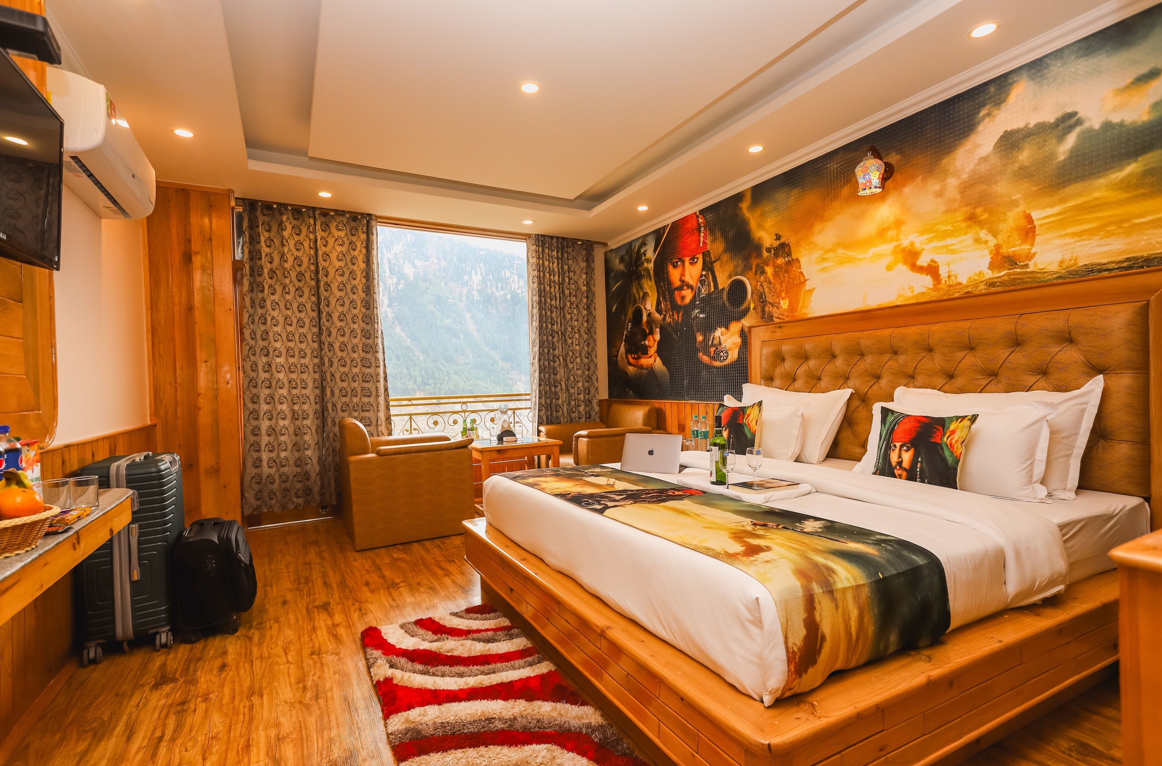 Habitación de hotel con una cama grande, un escritorio con equipaje, una silla y vistas a montañas a través de la ventana.