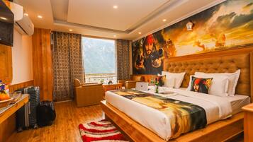 Habitación de hotel con una cama grande, un escritorio con equipaje, una silla y vistas a montañas a través de la ventana.