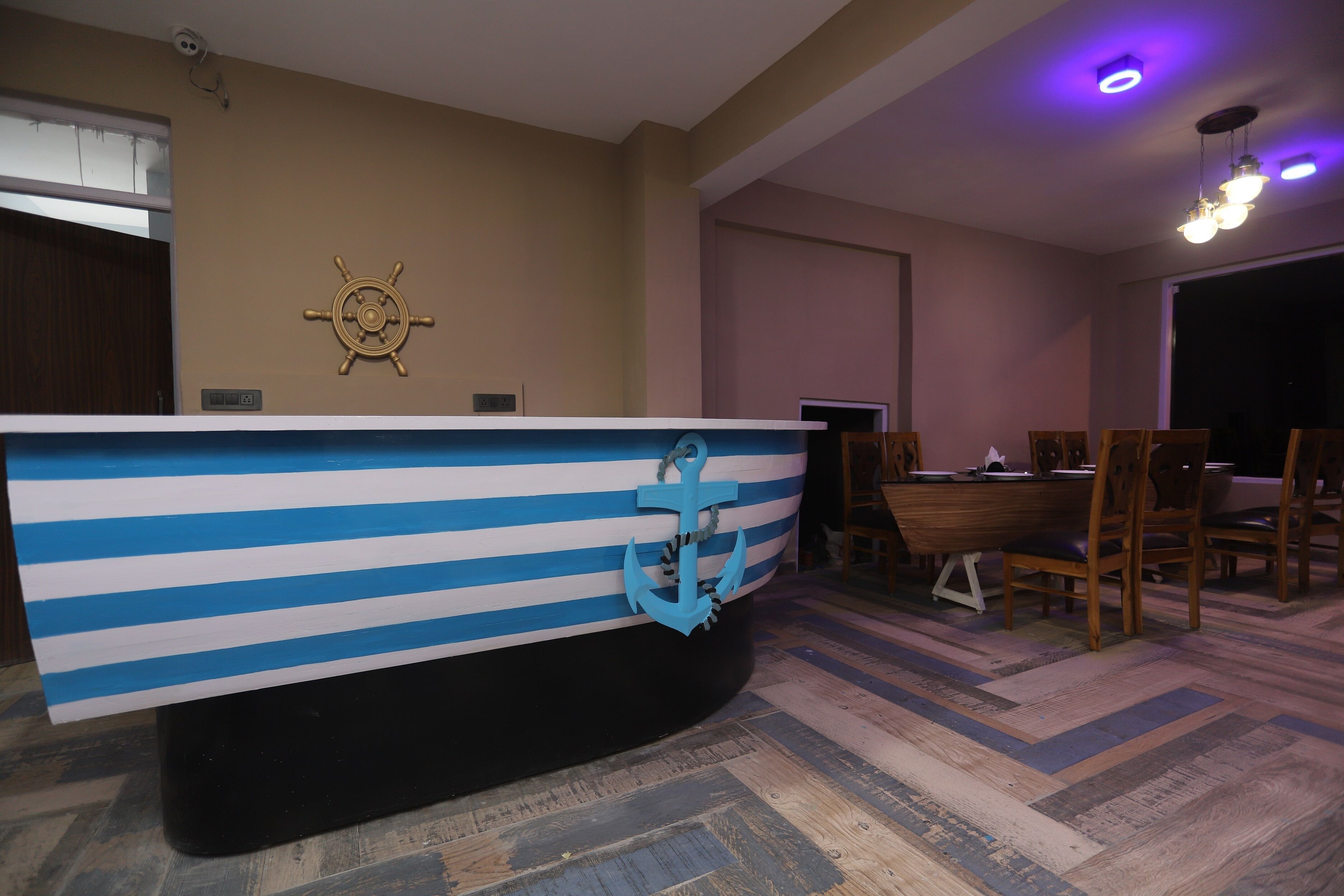 Una habitación con una mesa grande y a rayas con forma de barco en el centro, una rueda de barco en la pared y un comedor con sillas y una mesa.