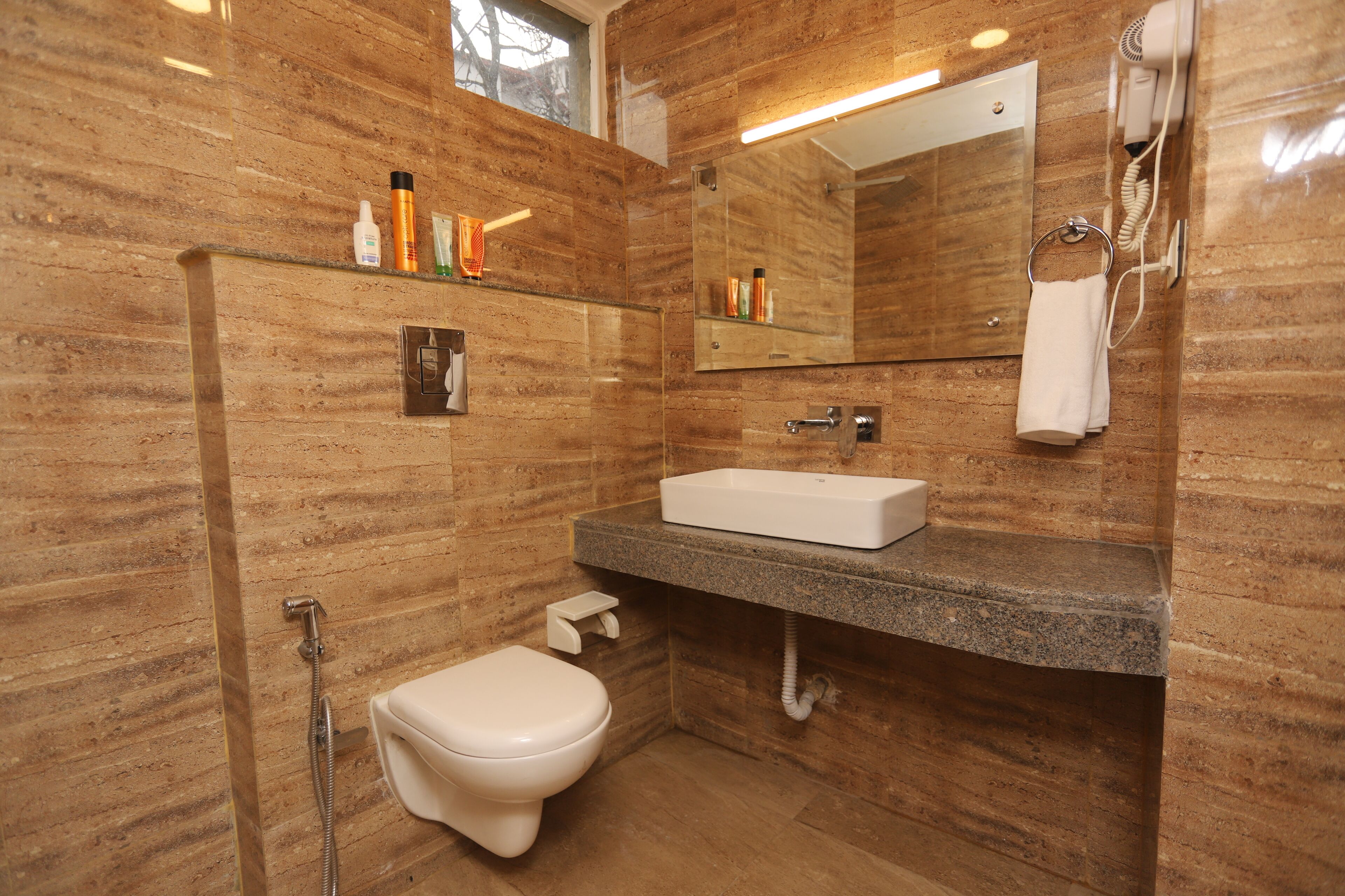 Un baño con pared de mármol, un lavamanos blanco, un espejo y un perchero para toallas.
