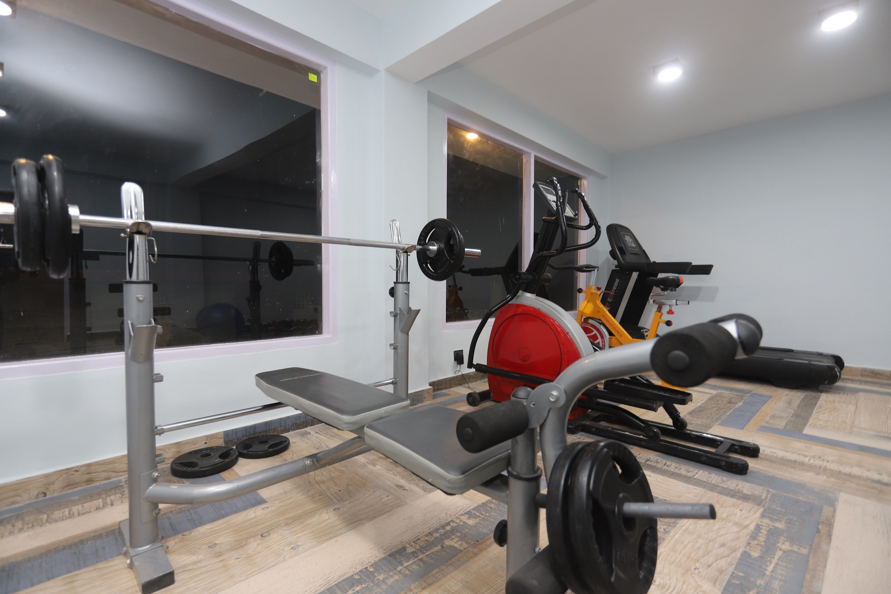 A gym with a bench press, weight bench, and a treadmill.