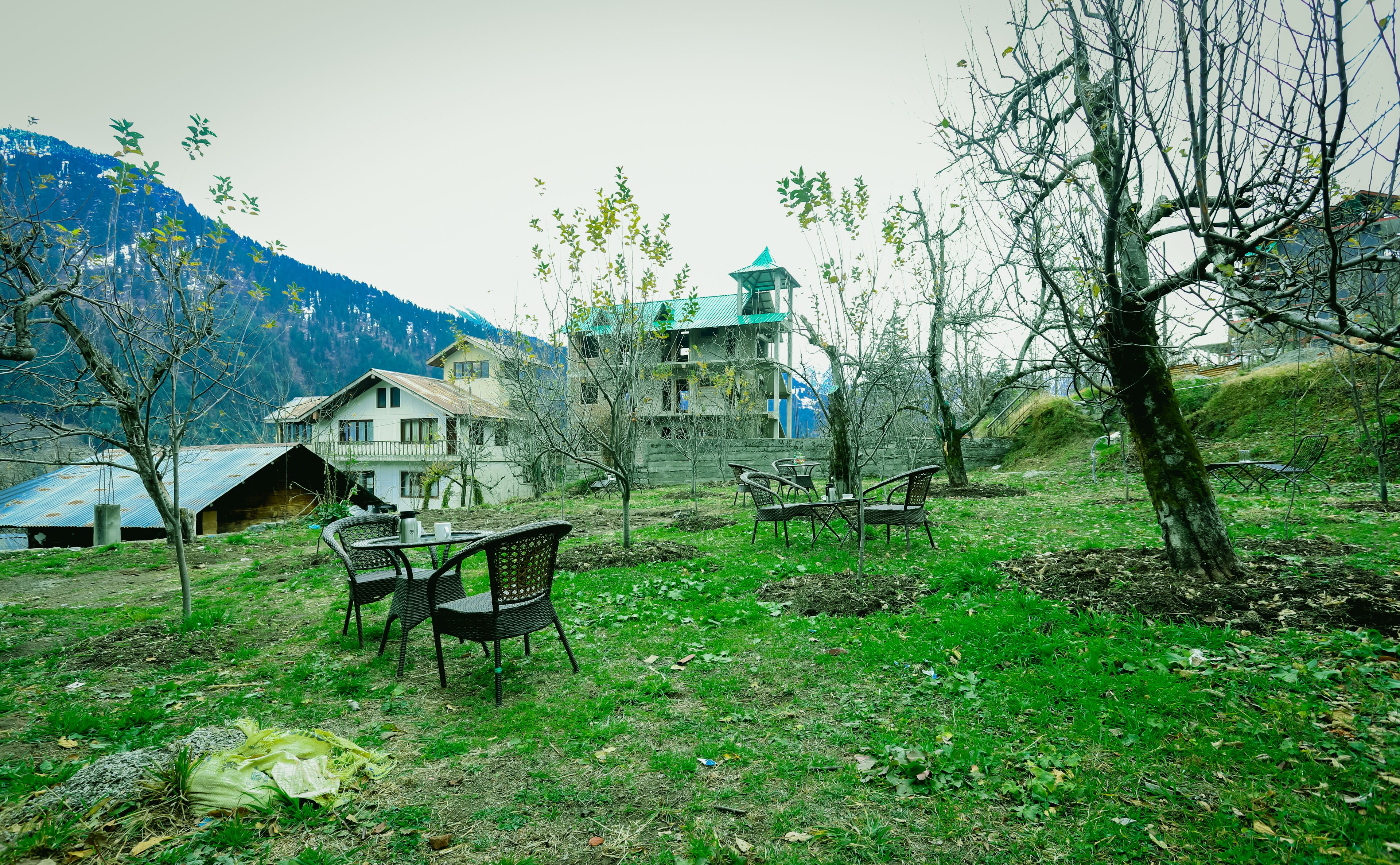 A rustic house with a balcony, surrounded by trees and a mountain backdrop.