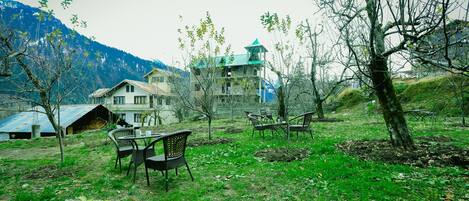 A rustic house with a balcony, surrounded by trees and a mountain backdrop.