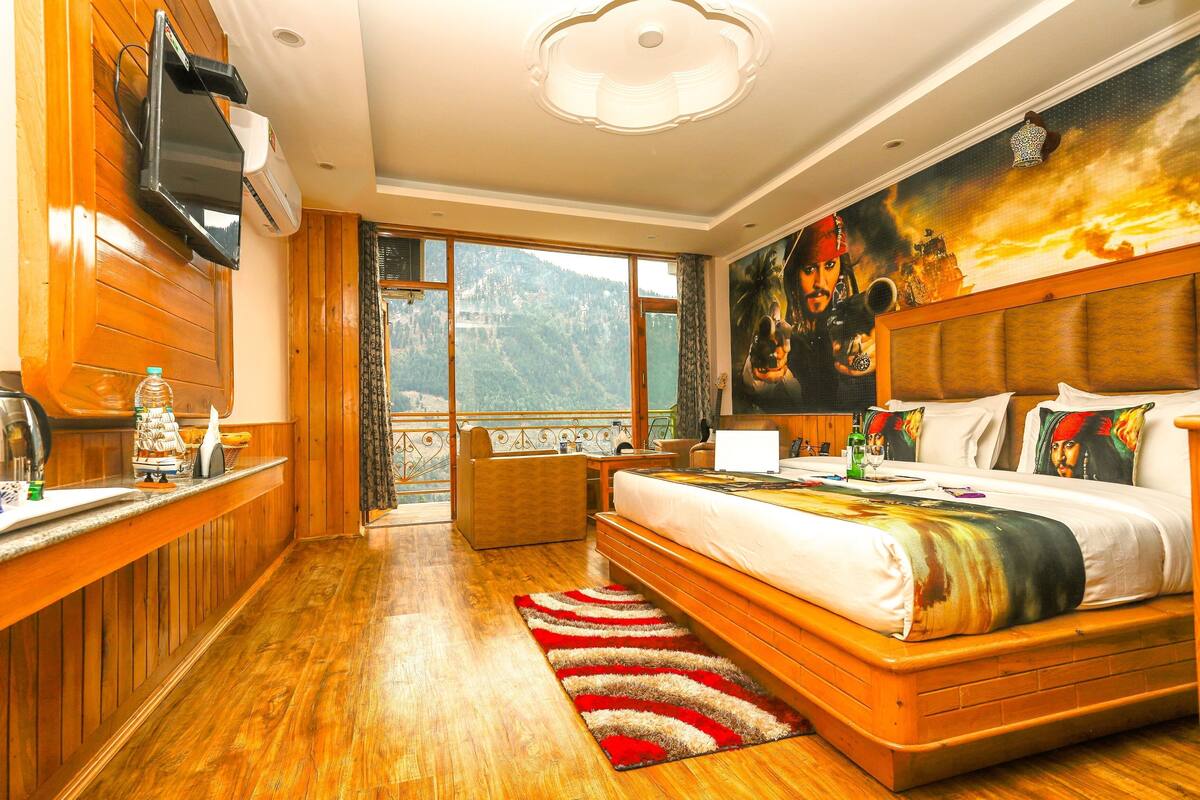 A hotel room with a large bed, a television, a desk with a computer, and a view of the mountains.